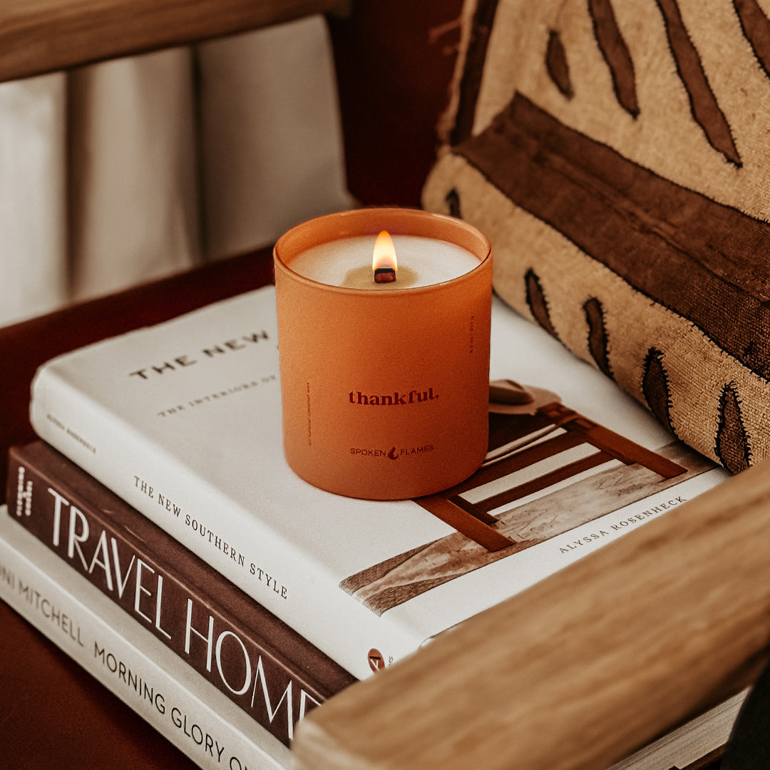 Spoken Flames Candle labeled 'thankful' on a stack of books with a cozy background